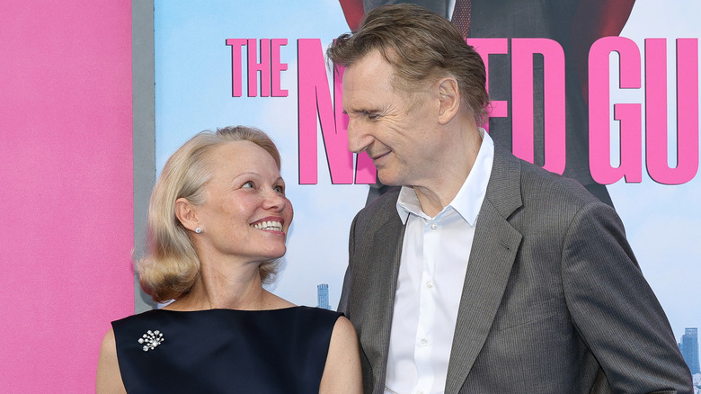 Pamela Anderson and Liam Neeson smiling at each other on the red carpet.
