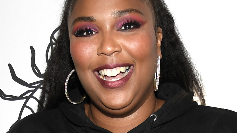 Lizzo smiles wearing hoop earrings