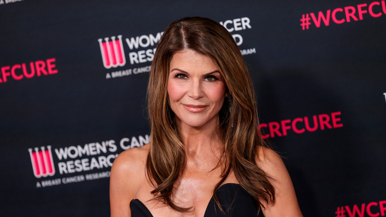 Lori Loughlin smiling while posing on the red carpet in a black strapless dress