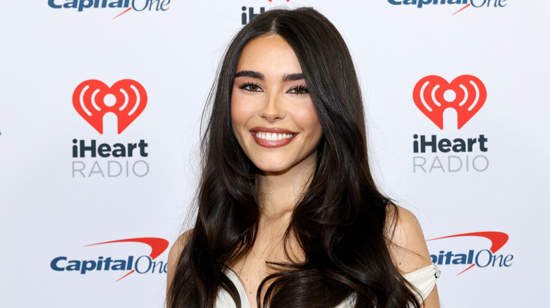 Madison Beer wearing an off the shoulder white dress while smiling on the red carpet