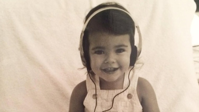 A baby Madison Beer with large headphones on her head smiling at the camera