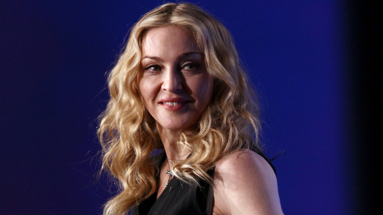 Madonna, with long blonde hair, smiling in front of a blue blackground