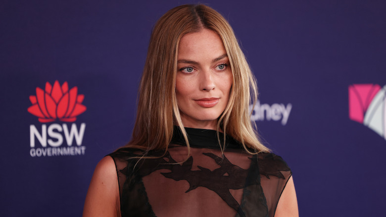 Margot Robbie in a floral dress, with a neutral expression, during a panel interview