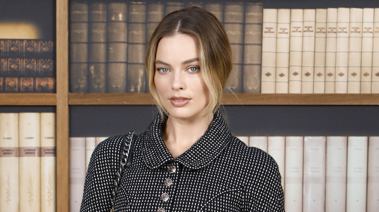 Margot Robbie in a black-and-white outfit, standing in front of books