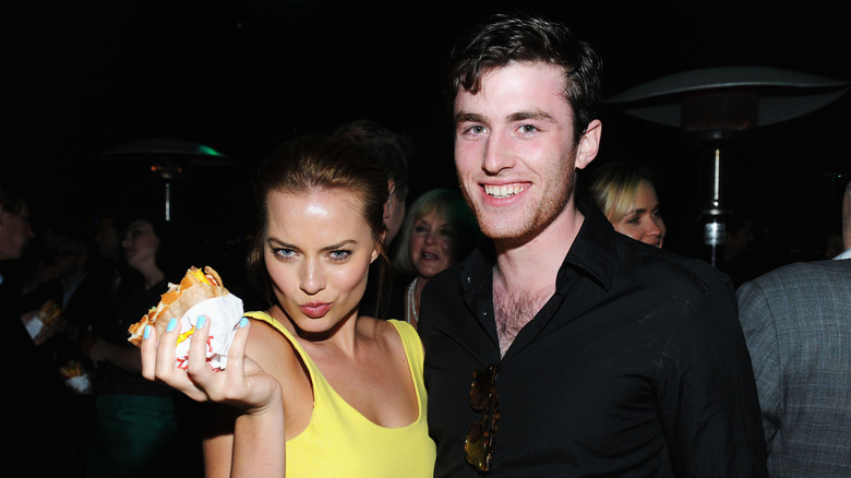 Margot Robbie holding a burger, making a funny face