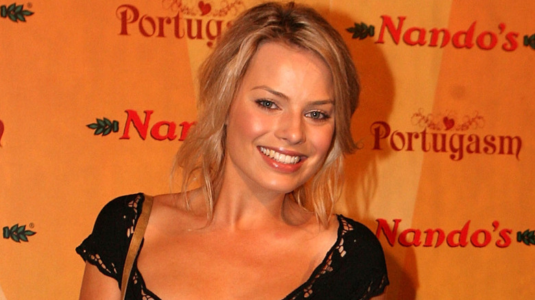 Margot Robbie in a black dress with a big smile