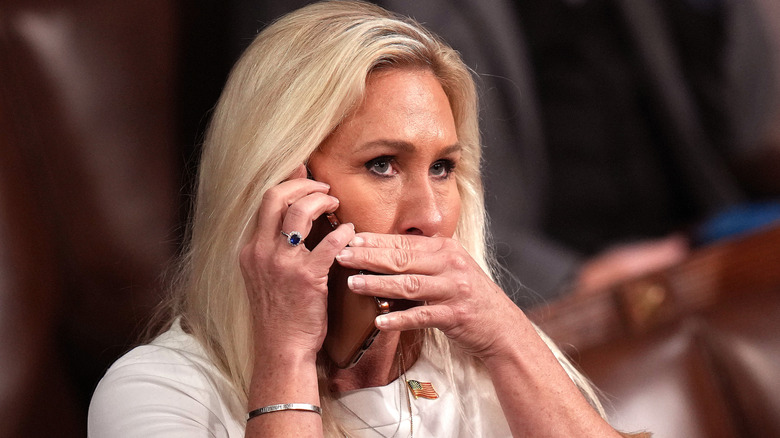 Marjorie Taylor Greene covers her mouth while speaking on the phone.