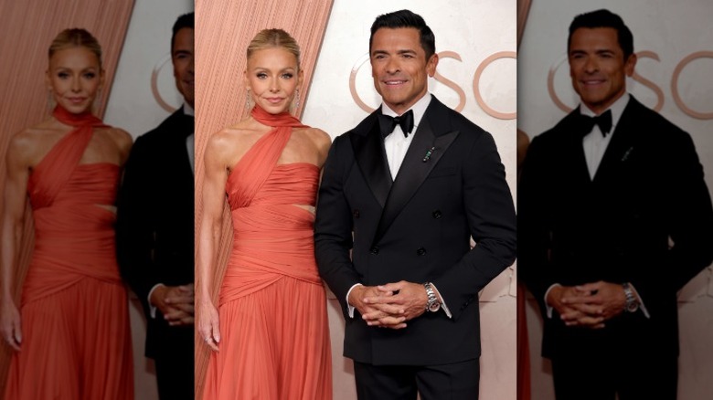 Kelly Ripa stands with her shoulder slightly behind that of Mark Consuelos, who has his hands clasped in front of him.