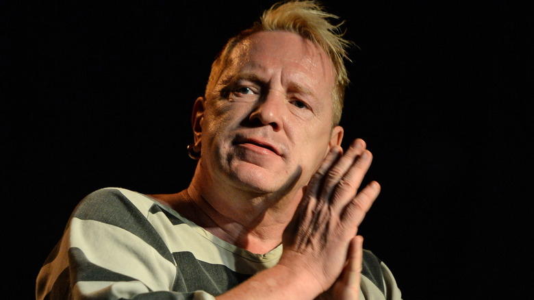 Johnny Rotten, in a prison style shirt, hands clasped