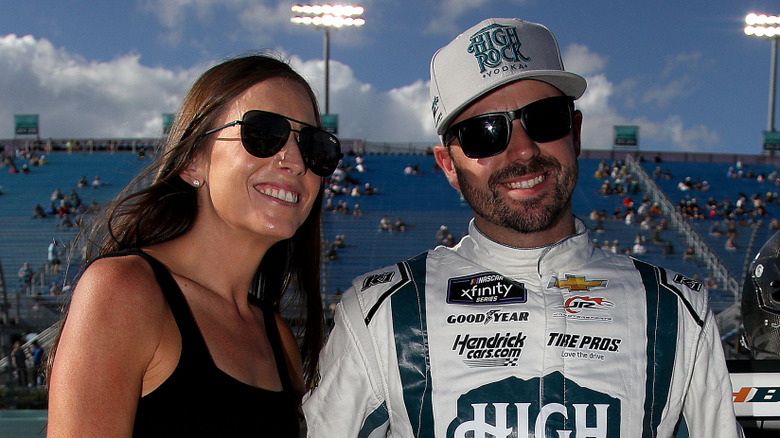 Josh Berry and Ginny Berry smiling together while wearing sunglasses beside a racetrack