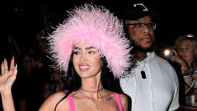 Megan Fox wearing a pink feather hat and waving