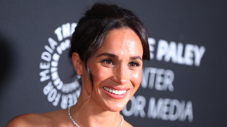 Meghan Markle smilling and wearing a diamond necklace