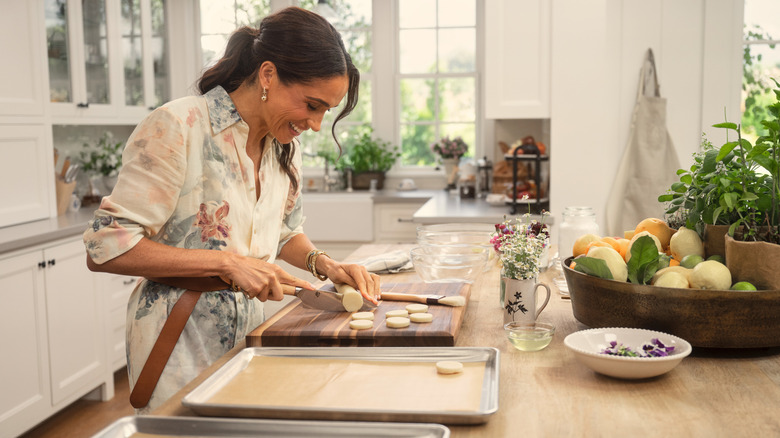 Meghan Markle smiling and slicing in her kitchen during Season 1 in a Ralph Lauren dress