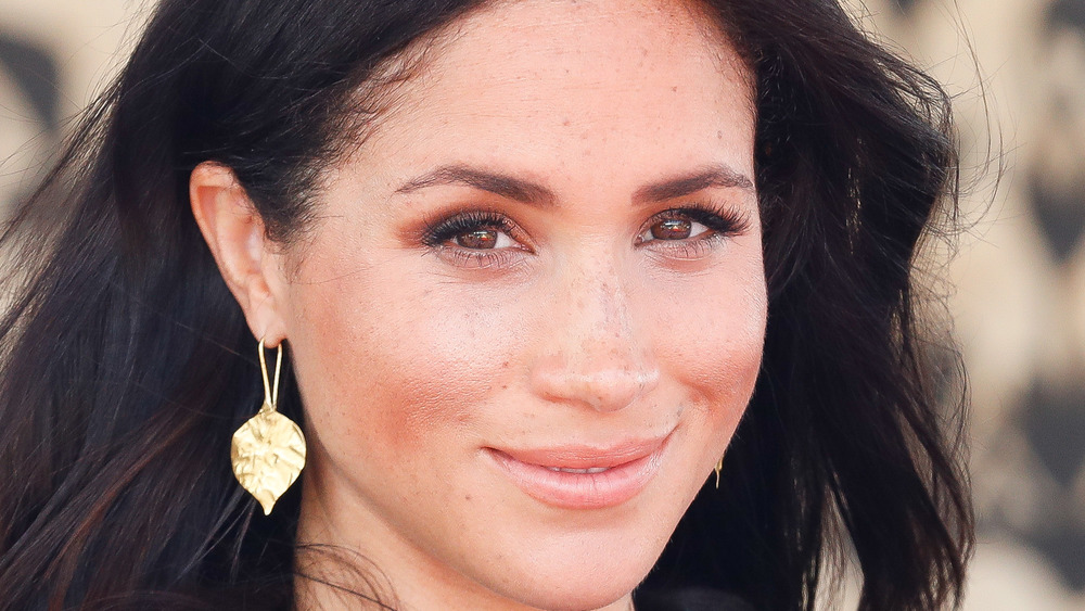 Meghan Markle smiling while wearing gold leaf earrings