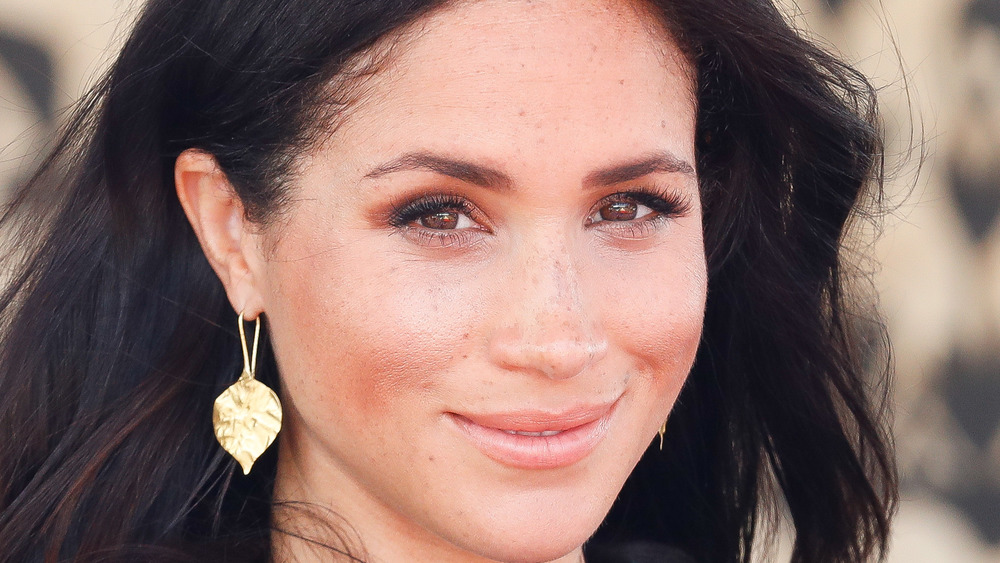 Meghan Markle smiling while wearing gold leaf earrings