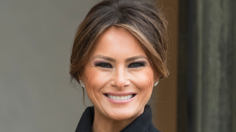 Melania Trump smiles and wears her hair in an updo