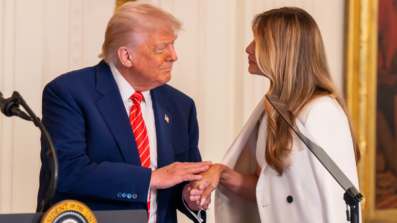 Donald Trump awkwardly patting Melania Trump's hand as he welcomes her on stage at an event for military mothers.
