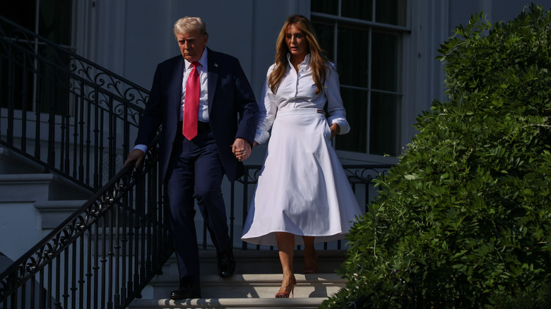 Donald and Melania Trump walking down stairs holding hands