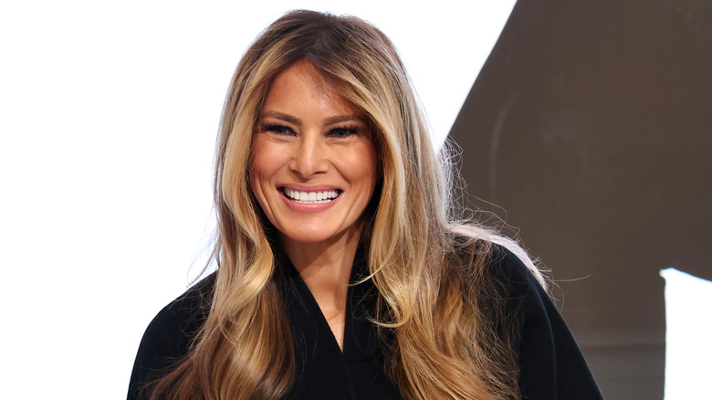 Melania Trump smiling showing teeth in black outfit