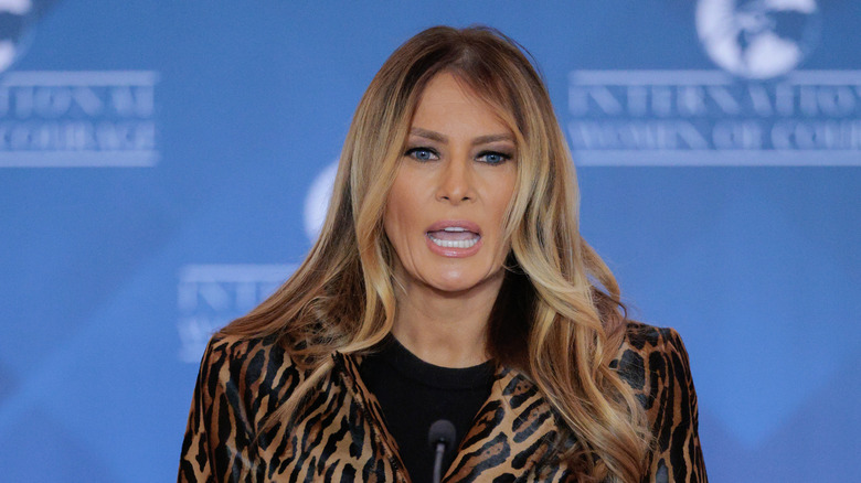 Melania Trump standing at a microphone in a leopard print coat