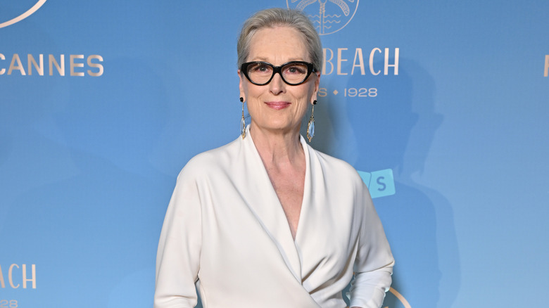 Meryl Streep smiling while wearing a white dress and glasses with black frames.