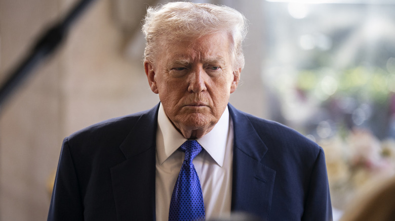 Donald Trump pictured at Mar-a-Lago in 2026 looking grumpy in a navy suit with a white shirt and a light blue tie