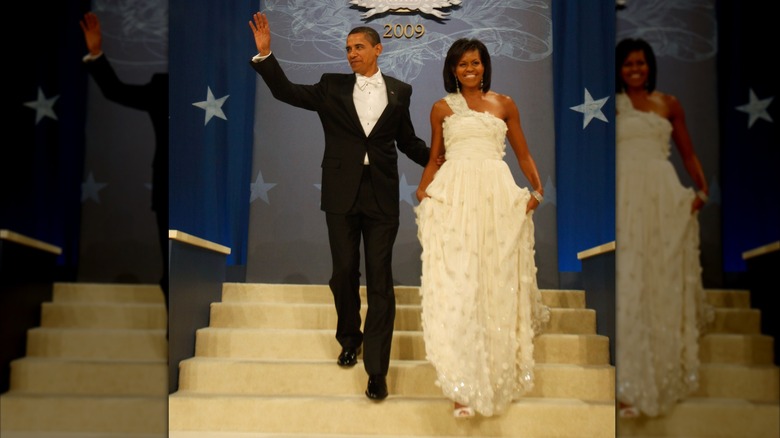 Michelle Obama holds onto her gown while walking down the steps, as Barack Obama waves.