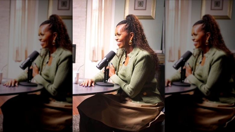 Michelle Obama smiles while sitting at a microphone