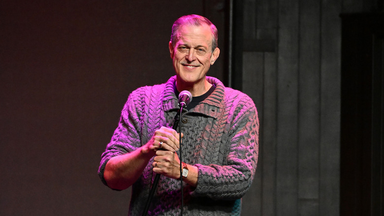 Billy Gardell holds a mic onstage during an April 2024 performance