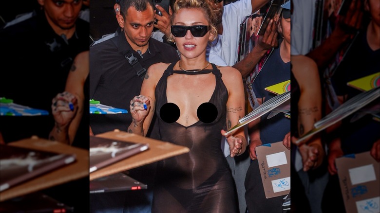 Miley Cyrus signing autographs while wearing a black see-through dress.