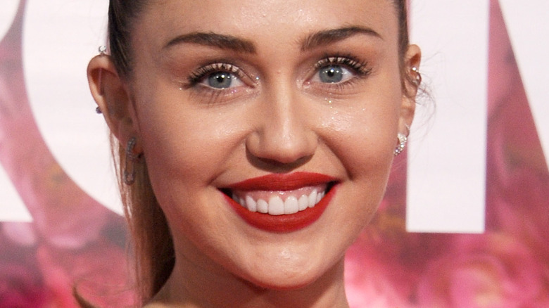 Miley Cyrus smiles on the red carpet with red lipstick