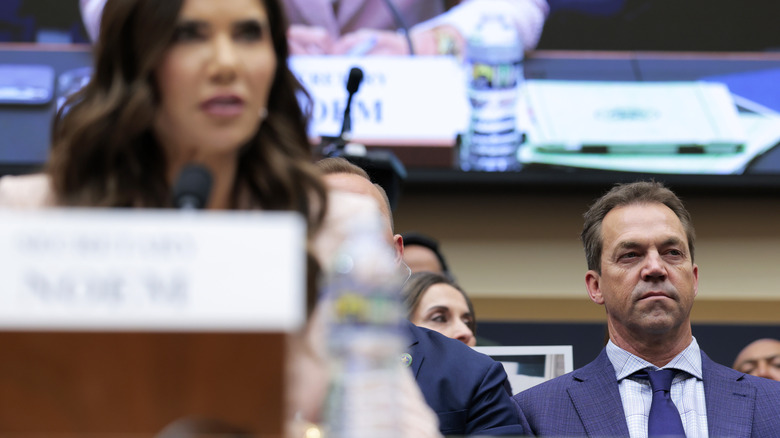 Bryon Noem seated behind Kristi Noem as she testifies