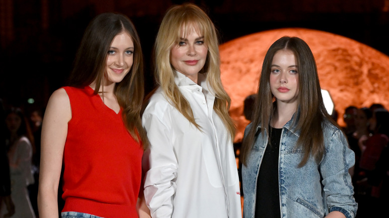 Nicole Kidman wearing a white button-up shirt and posing between her daughters Sunday and Faith