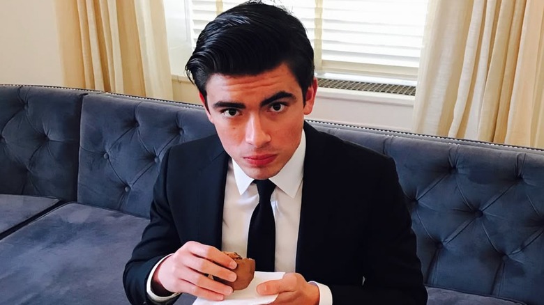 Michael Consuelos sitting on a couch holding a cookie.