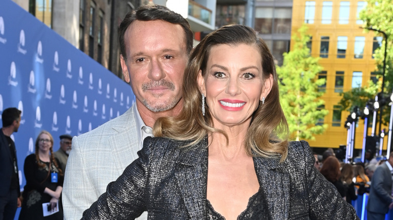 Tim McGraw wearing a grey suit holding the waist of Faith Hill wearing a black jacket and black lace dress