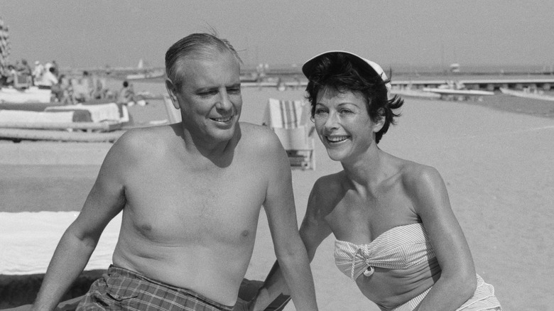 Hedy Lamarr, wearing a bikini, leans toward a topless William Howard Lee.