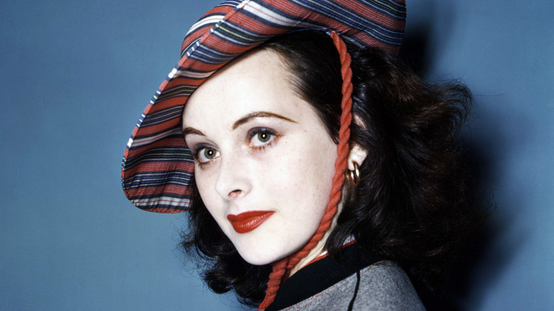 Hedy Lamarr, wearing a striped hat and striking makeup, gazes into the distance.