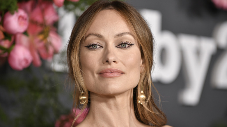 Olivia Wilde sports winged eyeliner and wears flower bud-shaped gold drop earrings.