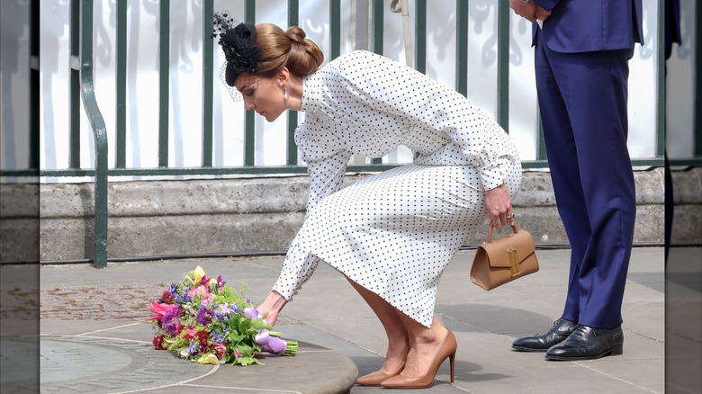 Kate Middleton in a polka dot dress bending down and placing flowers on a tomb