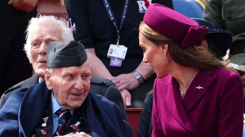 Kate Middleton wearing a bright pink hat with gig bow and talking to a war veteran