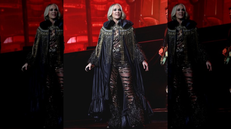 Carrie Underwood gazes into the distance, wearing a black outfit with yellow detailing.