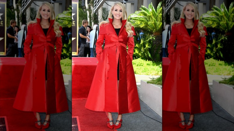 Carrie Underwood, wearing a striking red coat, poses with her hands in her pockets at her Hollywood Walk of Fame ceremony.