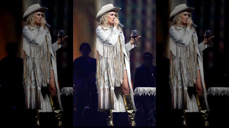 Carrie Underwood speaks into a microphone while holding a glass of wine.