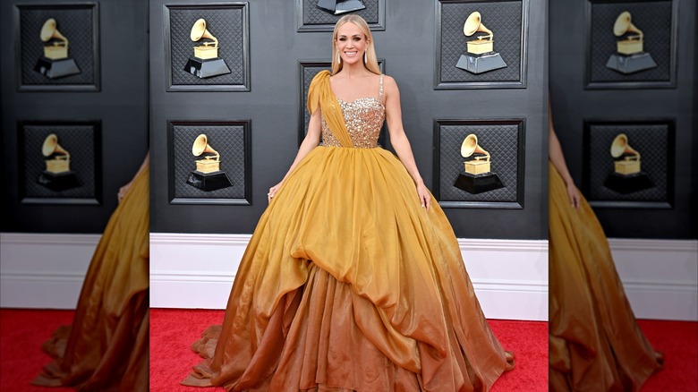 Carrie Underwood cheerfully displays a smile while wearing a burnt orange gown.