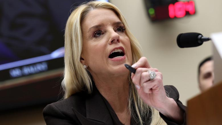 Pam Bondi speaking at a microphone and holding a pen up.