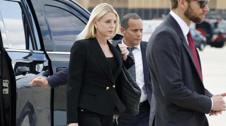 Pam Bondi looking downcast while wearing an all-black suit as she steps out of a car