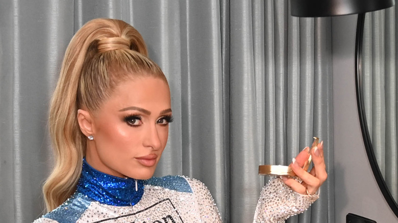 Paris Hilton posing in a chair with a compact out