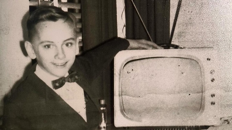 Young Pat Sajak posing next to a TV