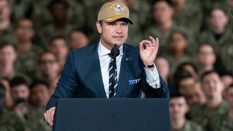 Pete Hegseth addressing a crowd while raising his hand
