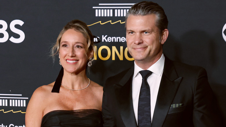 Jennifer Hegseth, wearing a strapless black dress, and husband Pete Hegseth, wearing a black suit and black tie, smiling.